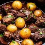 Crockpot garlic butter perfection with tender beef chunks and golden potatoes in rich garlic butter sauce, garnished with fresh parsley in a white ceramic slow cooker bowl