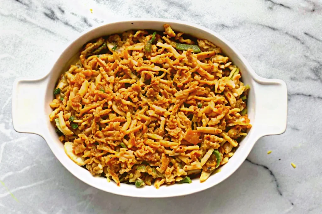Classic green bean casserole with crispy French fried onions on top, served in a white baking dish, showing the creamy mushroom sauce coating tender green beans