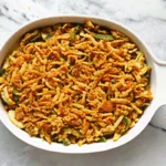 Classic green bean casserole with crispy French fried onions on top, served in a white baking dish, showing the creamy mushroom sauce coating tender green beans