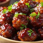 Golden mini meatballs in cranberry BBQ sauce garnished with fresh herbs on white ceramic serving platter with colorful toothpicks