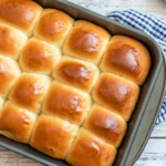 Golden brown homemade dinner rolls arranged in baking pan, freshly baked and brushed with melted butter