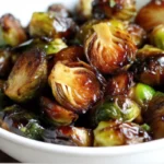 "Crispy honey balsamic brussels sprouts with golden caramelized edges and glossy balsamic glaze on a white serving platter, garnished with red pepper flakes