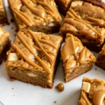 Fudgy Biscoff blondies with white chocolate chips cut into squares on parchment paper showing golden brown edges and soft centers