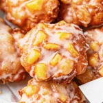 Golden brown Amish Apple Fritter with white glaze dripping down sides on rustic wooden plate with coffee cup