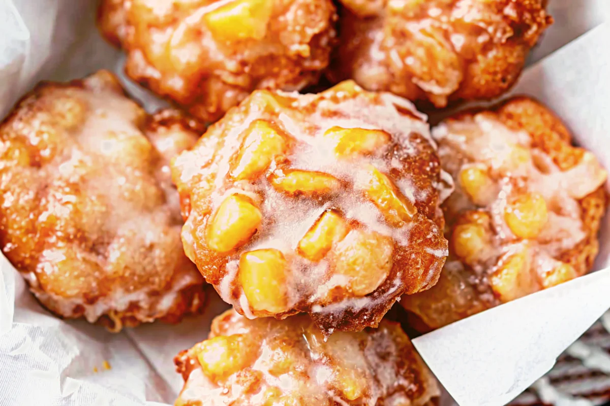 Golden brown Amish Apple Fritter with white glaze dripping down sides on rustic wooden plate with coffee cup