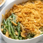 Golden gluten free green bean casserole with crispy fried onions and breadcrumb topping in white baking dish