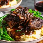 Fork-tender braised beef short ribs recipe with rich brown sauce, garnished with fresh herbs, served in rustic Dutch oven