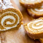 Sliced pumpkin roll cake showing spiral of orange pumpkin spice cake filled with white cream cheese frosting on white plate